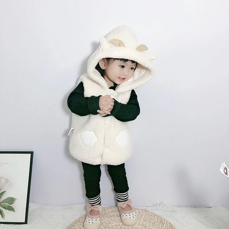 Toddler wearing a fluffy white hooded vest with animal ears over black outfit, standing indoors