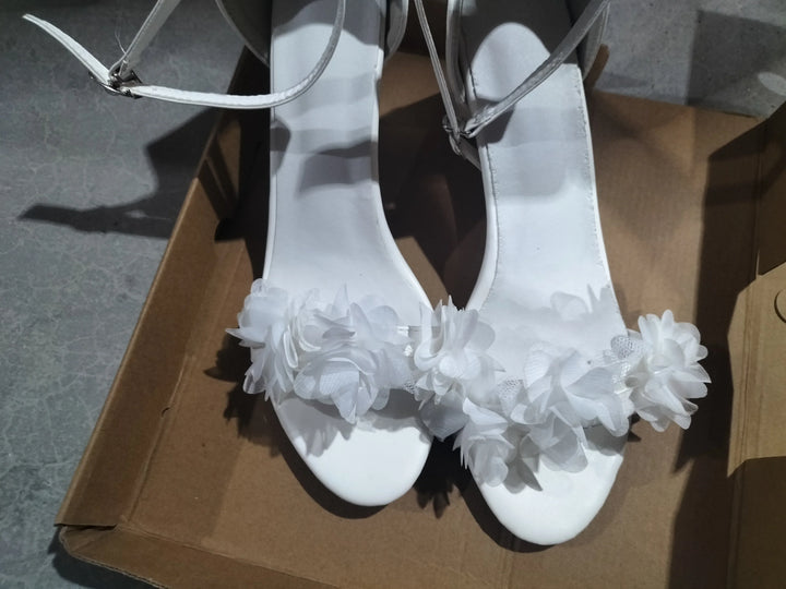 White women's high-heeled sandals with floral decorations on toe straps placed in a cardboard box
