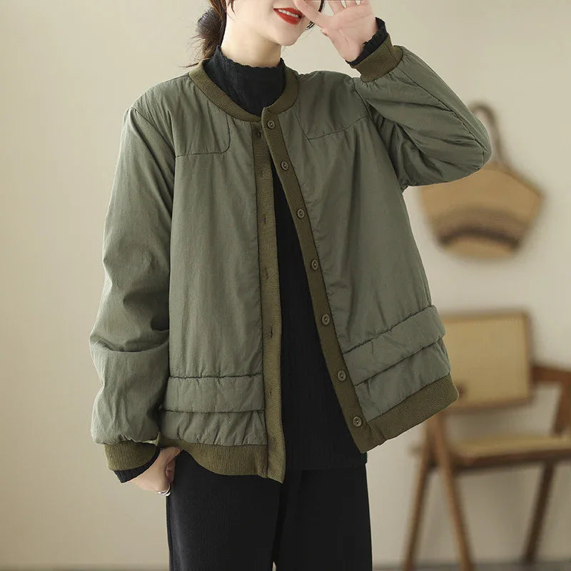 Woman wearing olive green buttoned bomber jacket over black outfit in minimalist indoor setting