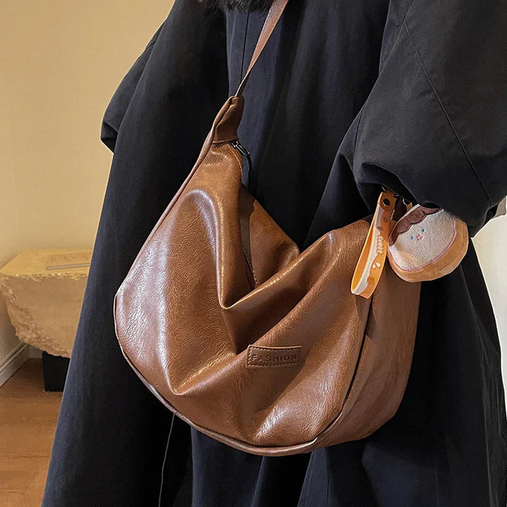 Brown leather shoulder bag with 'FASHION' label worn over black coat, decorated with cookie keychain