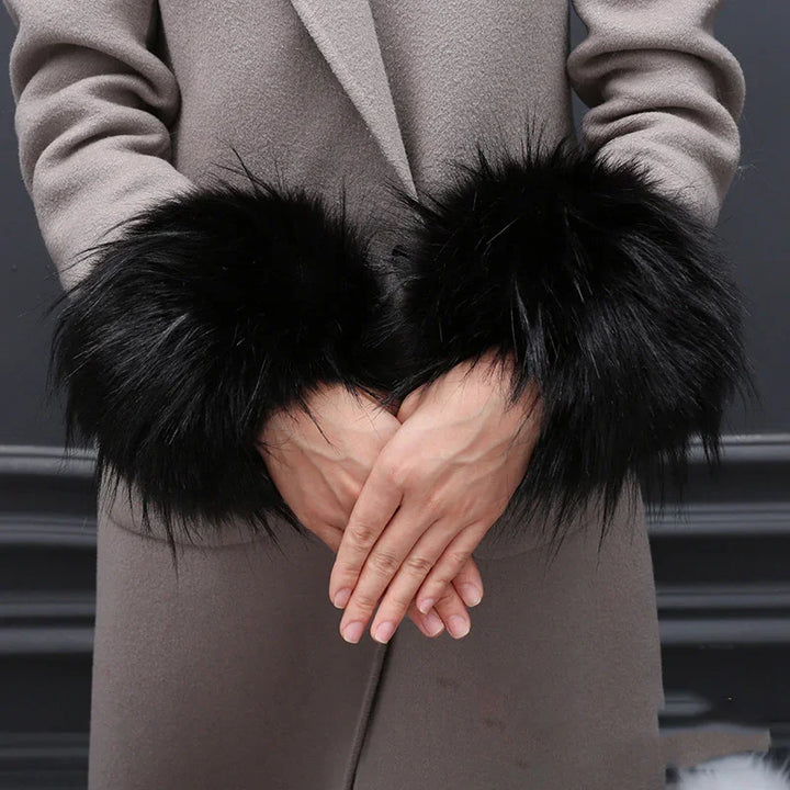 Person wearing gray coat with black fluffy fur cuffs on sleeve ends, hands clasped in front