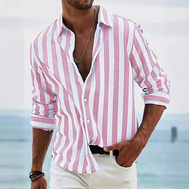 Man wearing pink and white vertical striped casual shirt with rolled-up sleeves near ocean