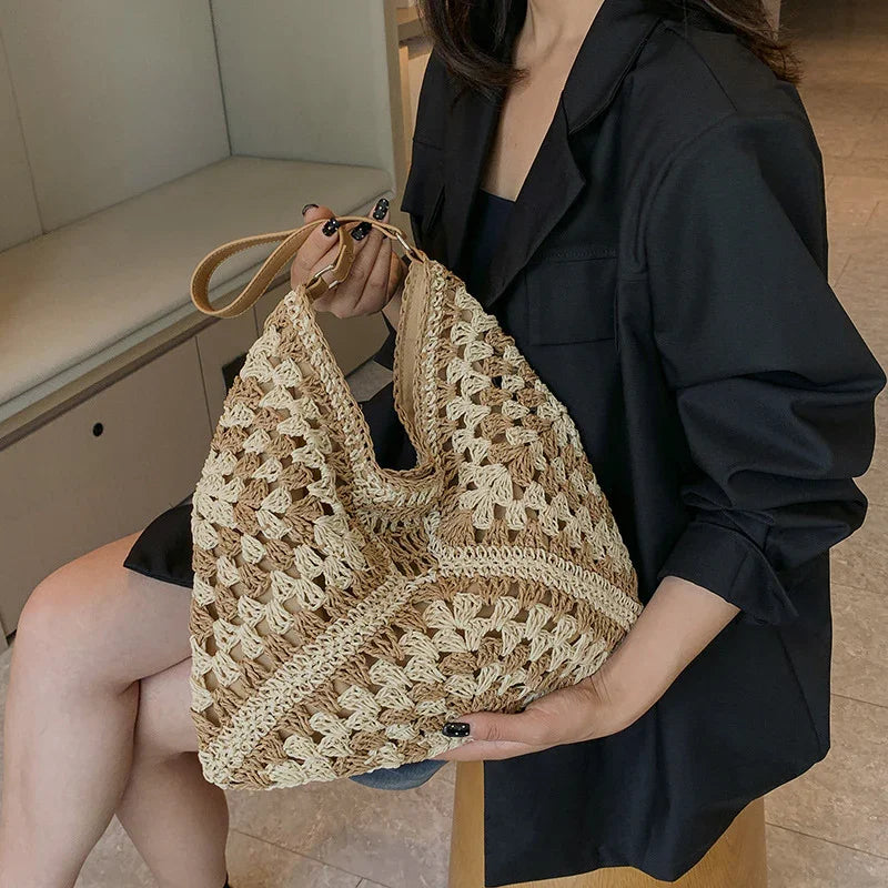 Woman holding beige and brown crocheted handbag with leather strap, wearing black blazer and shorts