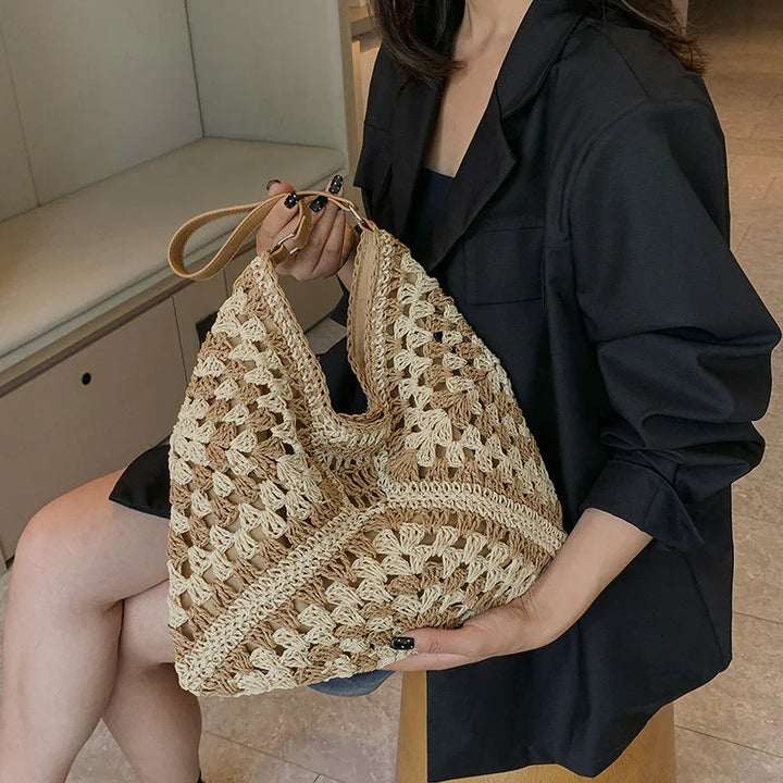 Woman holding beige and brown crocheted handbag with leather strap, wearing black blazer and shorts