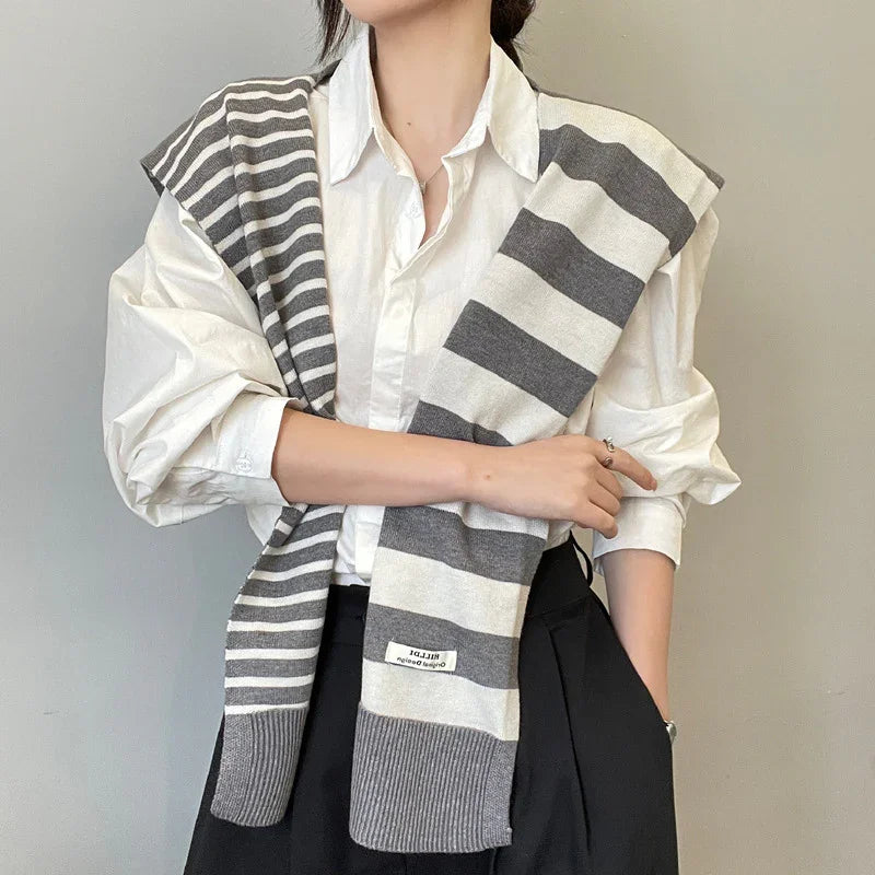 Person wearing white shirt with grey and white striped scarf draped over shoulders, black pants