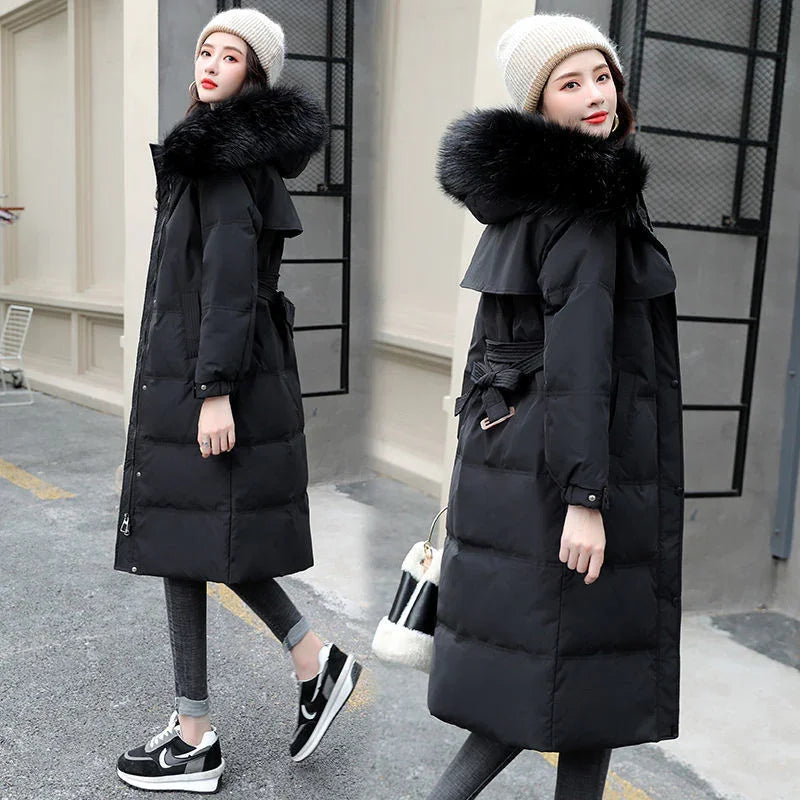 Woman wearing black long puffer coat with fur hood, beige knit hat, leggings, and black sneakers outdoors