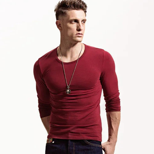 Young man wearing fitted long-sleeve red shirt and pendant necklace posing against white background