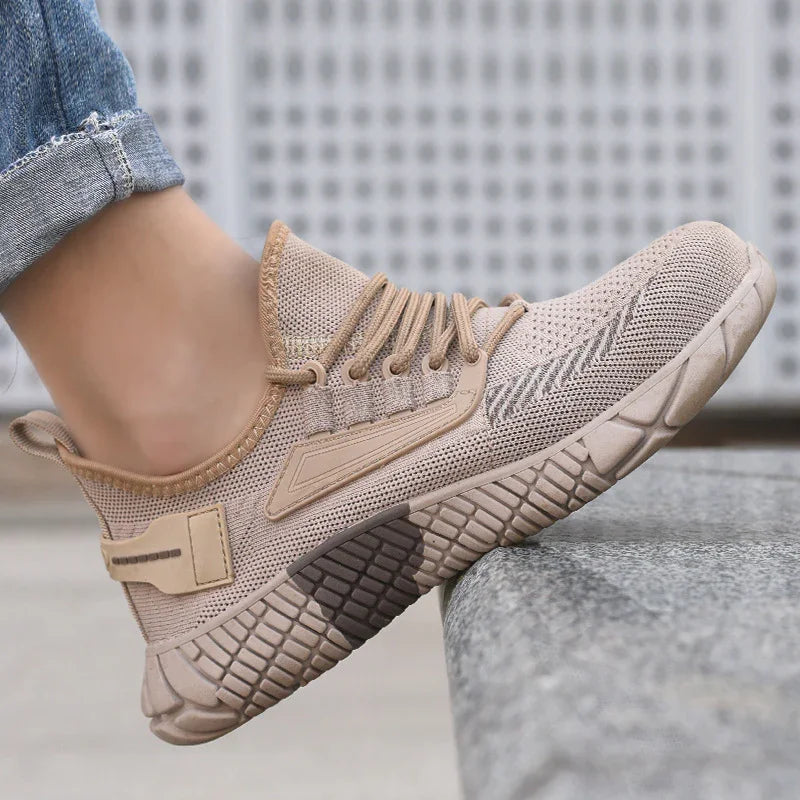 Beige knitted athletic shoe with textured sole worn with rolled blue jeans on stone surface