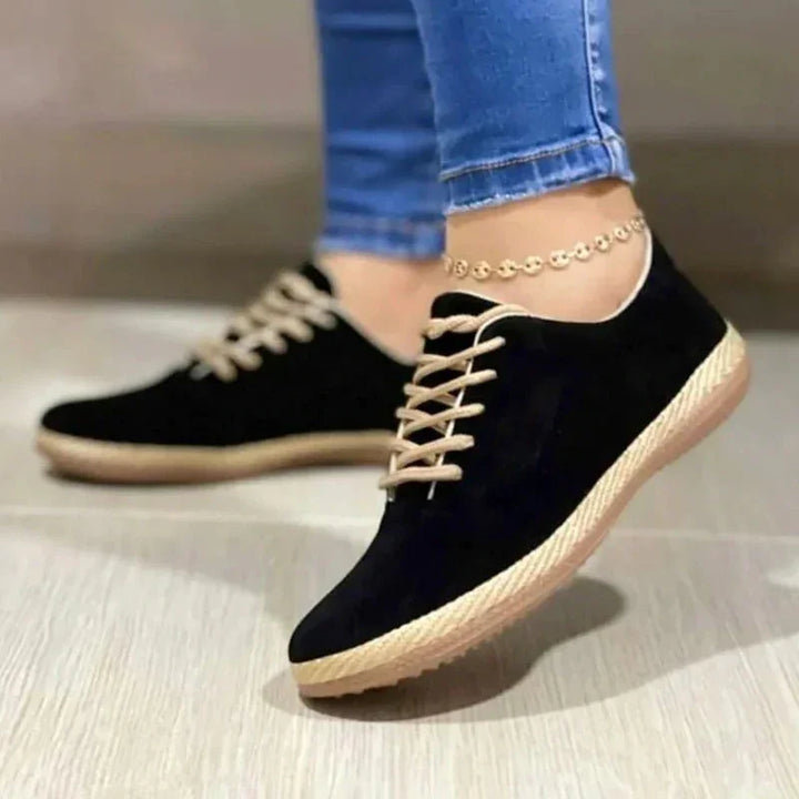 black casual sneakers with beige laces and soles worn with blue jeans and a gold anklet