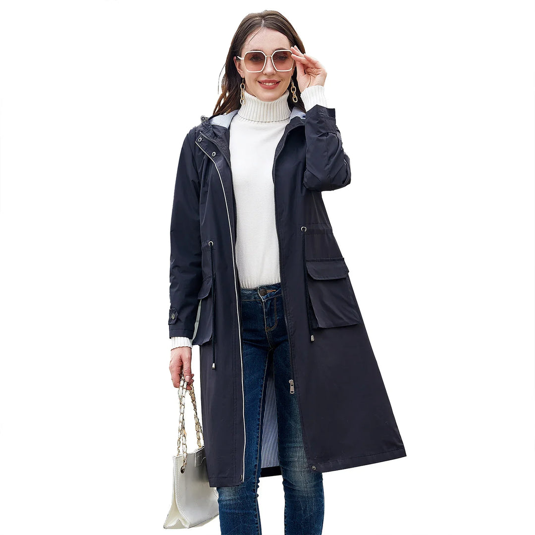 Woman wearing long black raincoat, white turtleneck sweater, blue jeans, sunglasses, holding white handbag