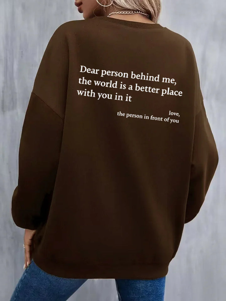 Woman wearing brown sweatshirt with white motivational quote on back against gray background