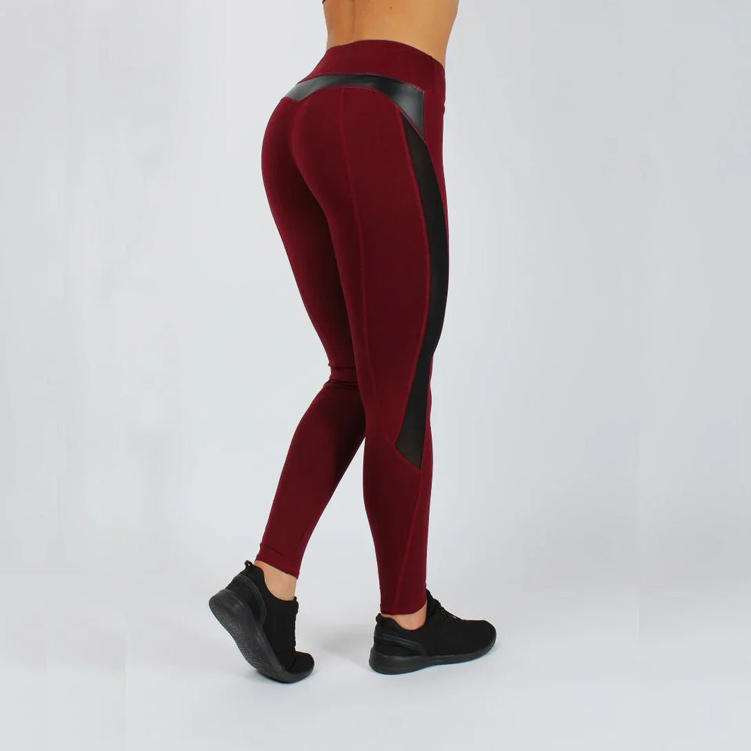 Woman wearing burgundy and black high-waisted athletic leggings, black sneakers, white background