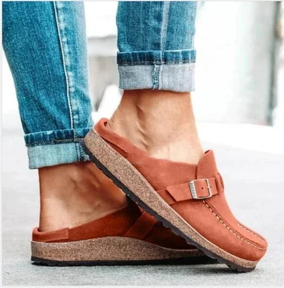 Person wearing brown suede slip-on clogs with buckle detail and cork soles paired with cuffed blue jeans