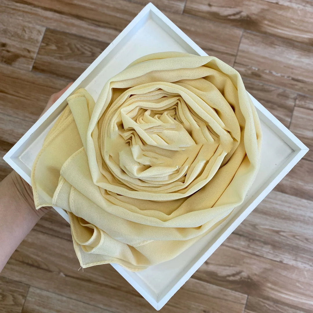 Hand holding round beige chiffon scarf in white square box on wooden floor