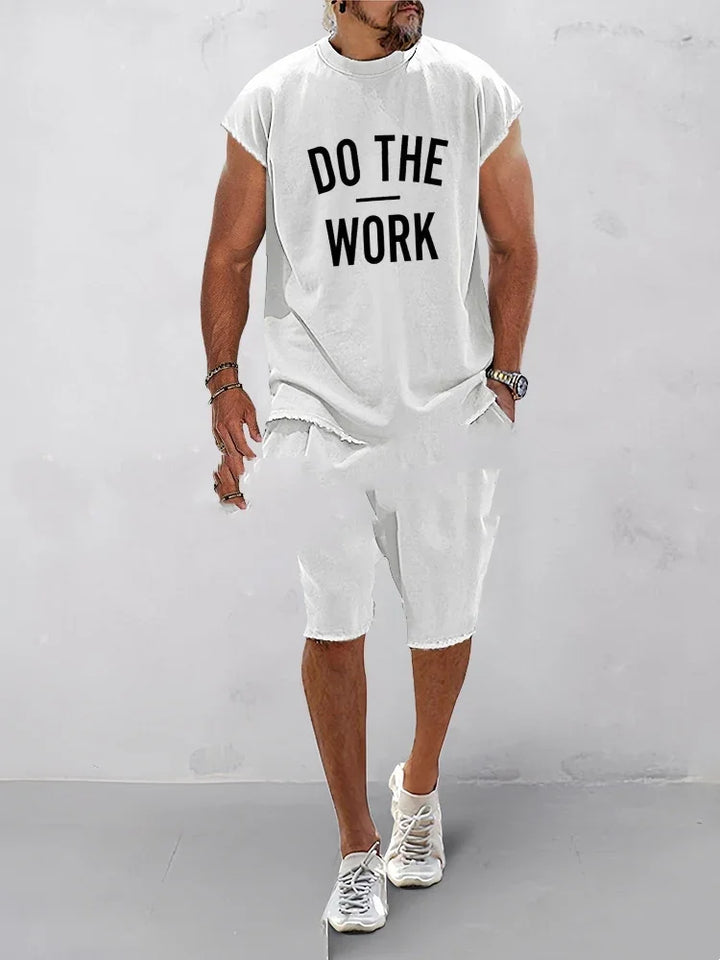 Man wearing white sleeveless shirt with Do The Work text and white shorts walking indoors
