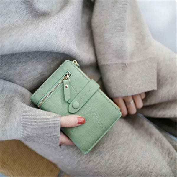 Close-up of hand holding a green suede wallet with zipper and snap button, wearing beige knitwear