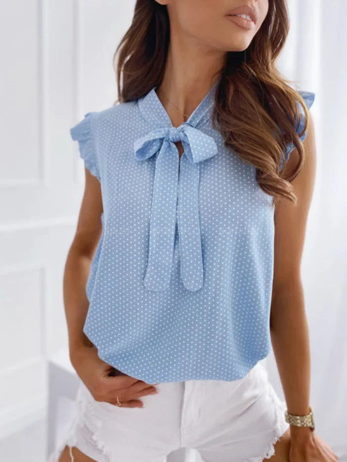 Woman wearing light blue polka dot sleeveless blouse with bow tie and white distressed shorts
