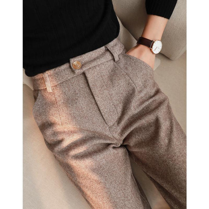 Close-up of person wearing high-waisted brown herringbone wool pants and black ribbed sweater with leather strap watch