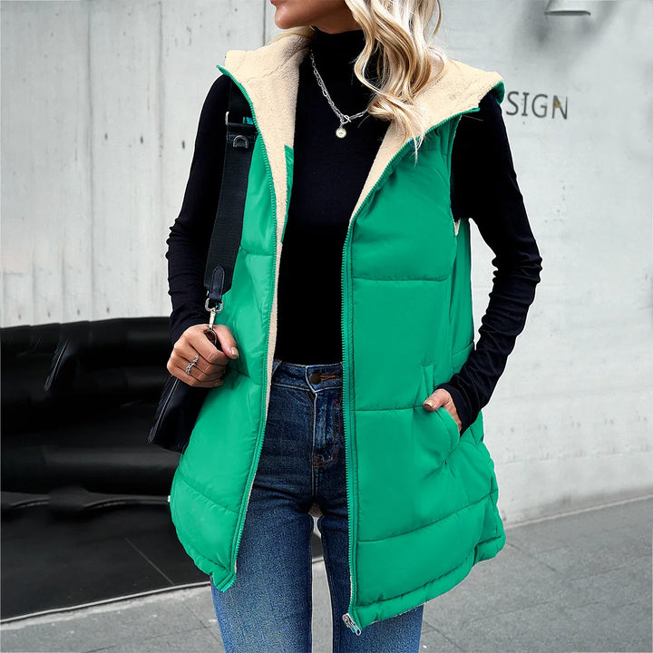 Woman wearing green sleeveless puffer vest with cream fleece lining, black turtleneck, and blue jeans outdoors