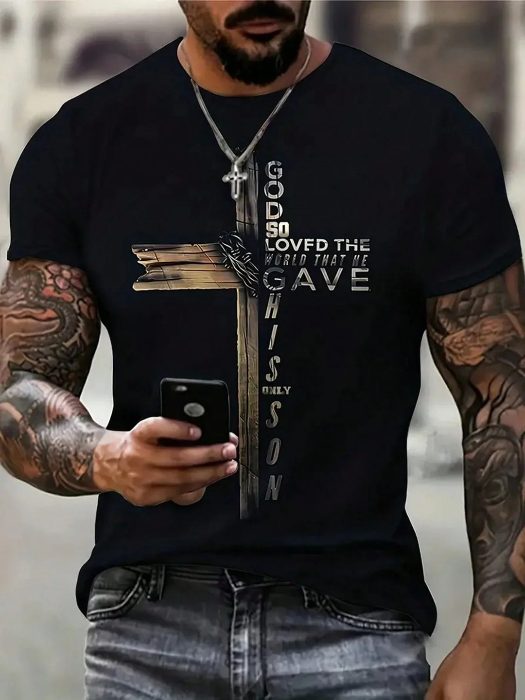 Muscular tattooed man wearing black t-shirt with wooden cross and Bible verse design holding smartphone