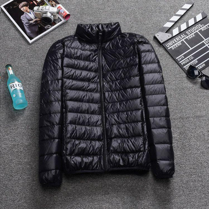 Black lightweight puffer jacket with zipper on gray carpet next to sunglasses, clapperboard, magazine, and blue RIO bottle