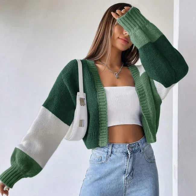 Woman wearing green and white color block cardigan with white crop top, light blue jeans, and white shoulder bag