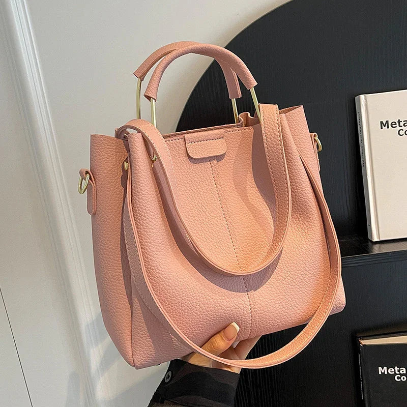 Hand holding a textured pink leather handbag with gold handles and long strap against black shelf background