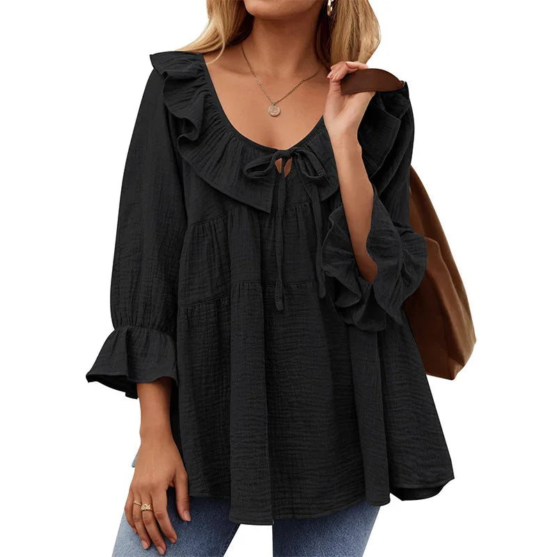 Woman wearing black ruffled long sleeve blouse with tie-neck detail and carrying brown bag