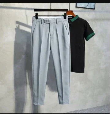 Light gray tailored pants with pleats and belt loops hanging beside black polo shirt with green collar and sleeve trim on wall