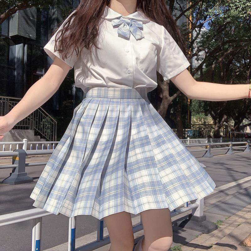Woman wearing blue plaid pleated skirt and white short-sleeve blouse with bow outdoors