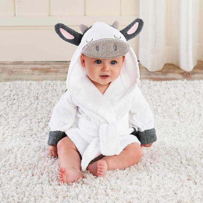 Baby sitting on plush white carpet wearing white cow-themed hooded bathrobe with ears and snout