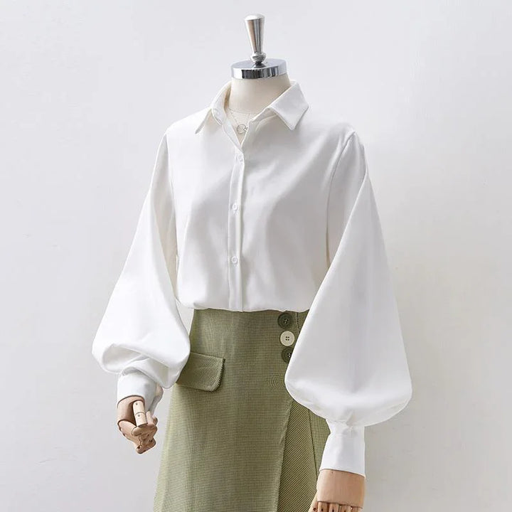 White blouse with balloon sleeves and green high-waisted skirt with buttons on mannequin