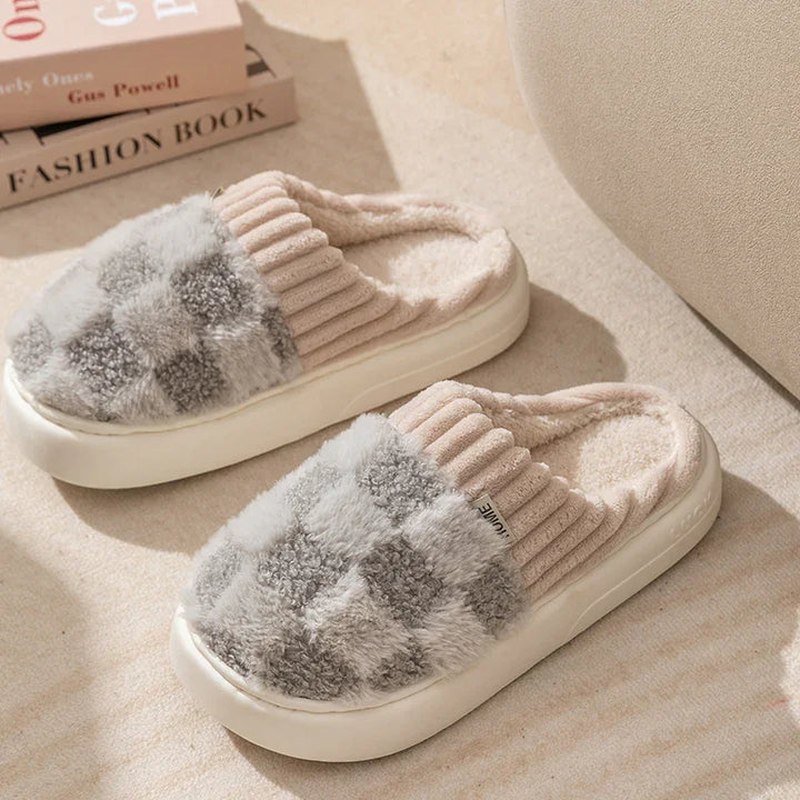 Cozy fuzzy slippers with grey and white checkerboard pattern and ribbed beige collar on beige carpet