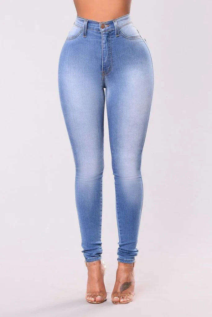 High-waisted light blue skinny jeans on model with transparent heels and ankle tattoo, studio background