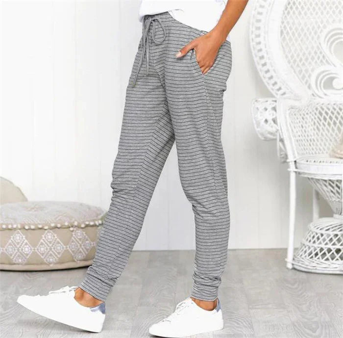 Woman wearing gray striped drawstring jogger pants with pockets and white sneakers in a cozy indoor setting
