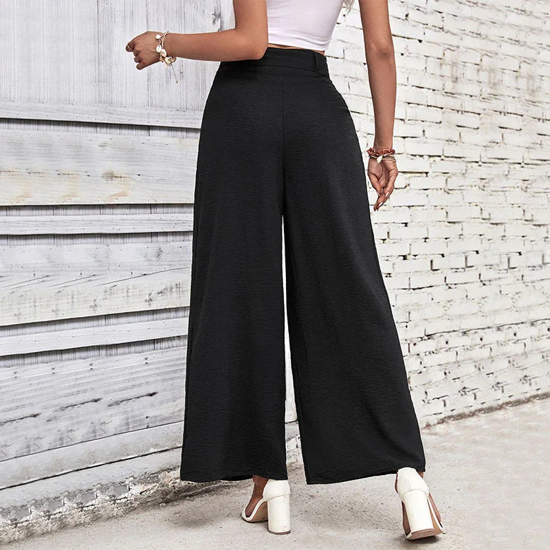 Woman wearing high-waisted black wide-leg pants with white block heel sandals against a brick wall