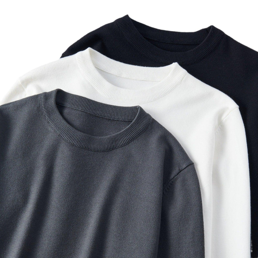 Three crewneck sweaters in black, white, and gray neatly layered on white background