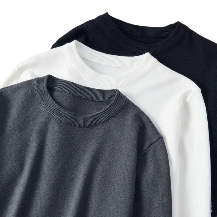 Three crewneck sweaters in black, white, and gray neatly layered on white background