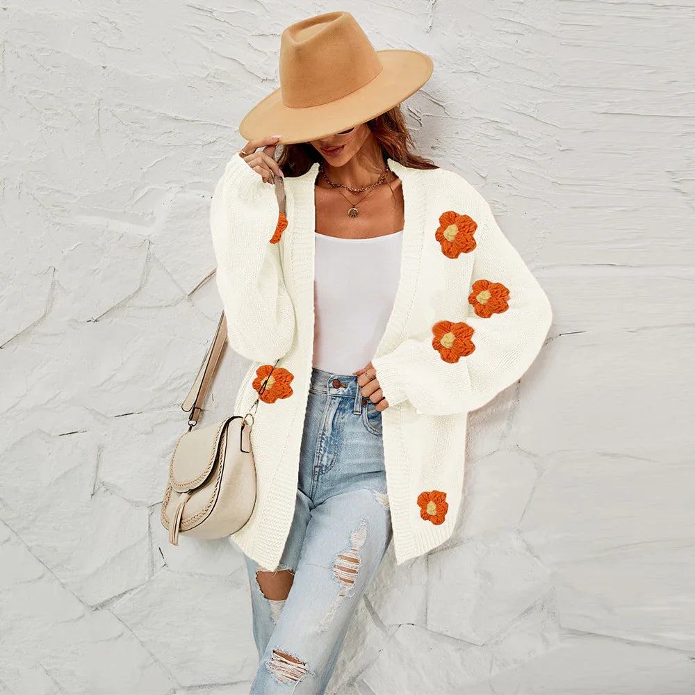 Woman wearing a white knitted cardigan with orange flower embroidery, ripped jeans, beige hat, and beige bag