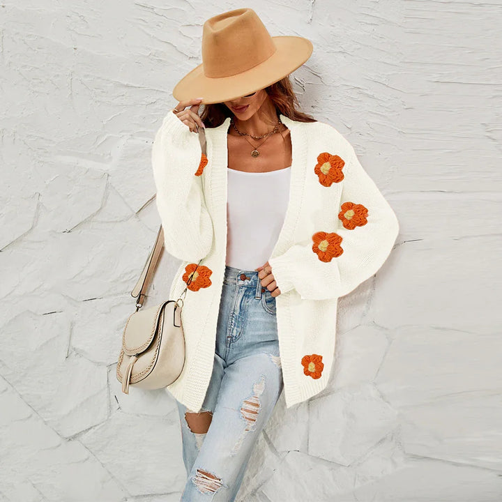 Woman wearing a white knitted cardigan with orange flower embroidery, ripped jeans, beige hat, and beige bag