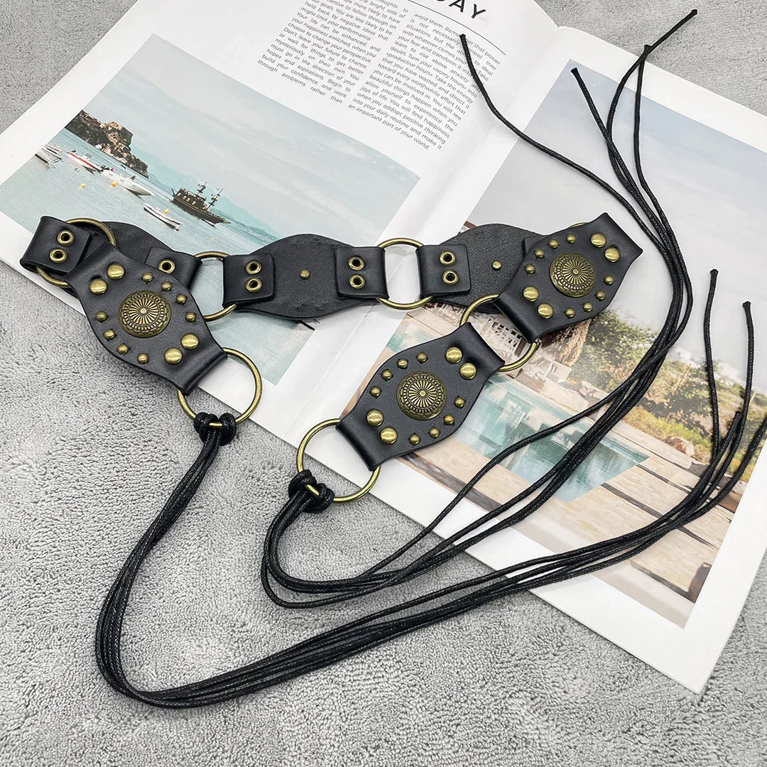 Black leather belt with brass studs and rings, laid on a textured gray surface over an open magazine