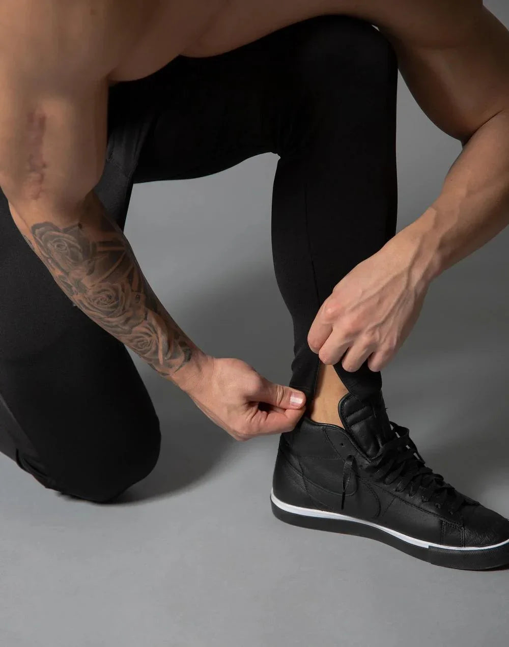 Athlete with tattooed arm wearing black leggings and black sneakers adjusting pant leg