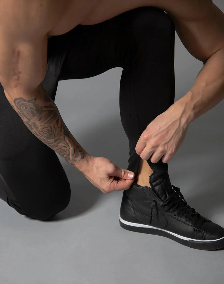 Athlete with tattooed arm wearing black leggings and black sneakers adjusting pant leg