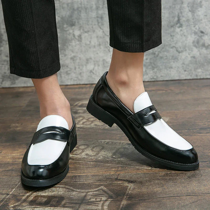 Close-up of black and white leather loafers worn with black pants on wooden floor