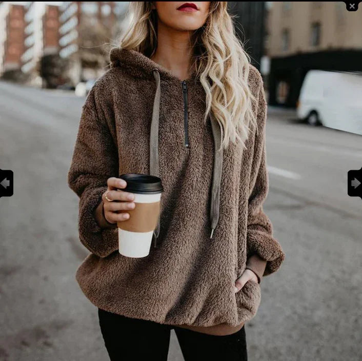 Woman wearing a cozy brown teddy fleece hoodie holding a coffee cup on a city street