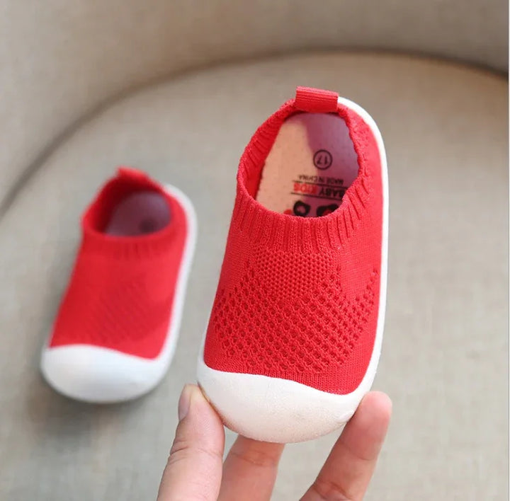 Close-up of red baby shoes with white rubber soles and knit texture on beige background