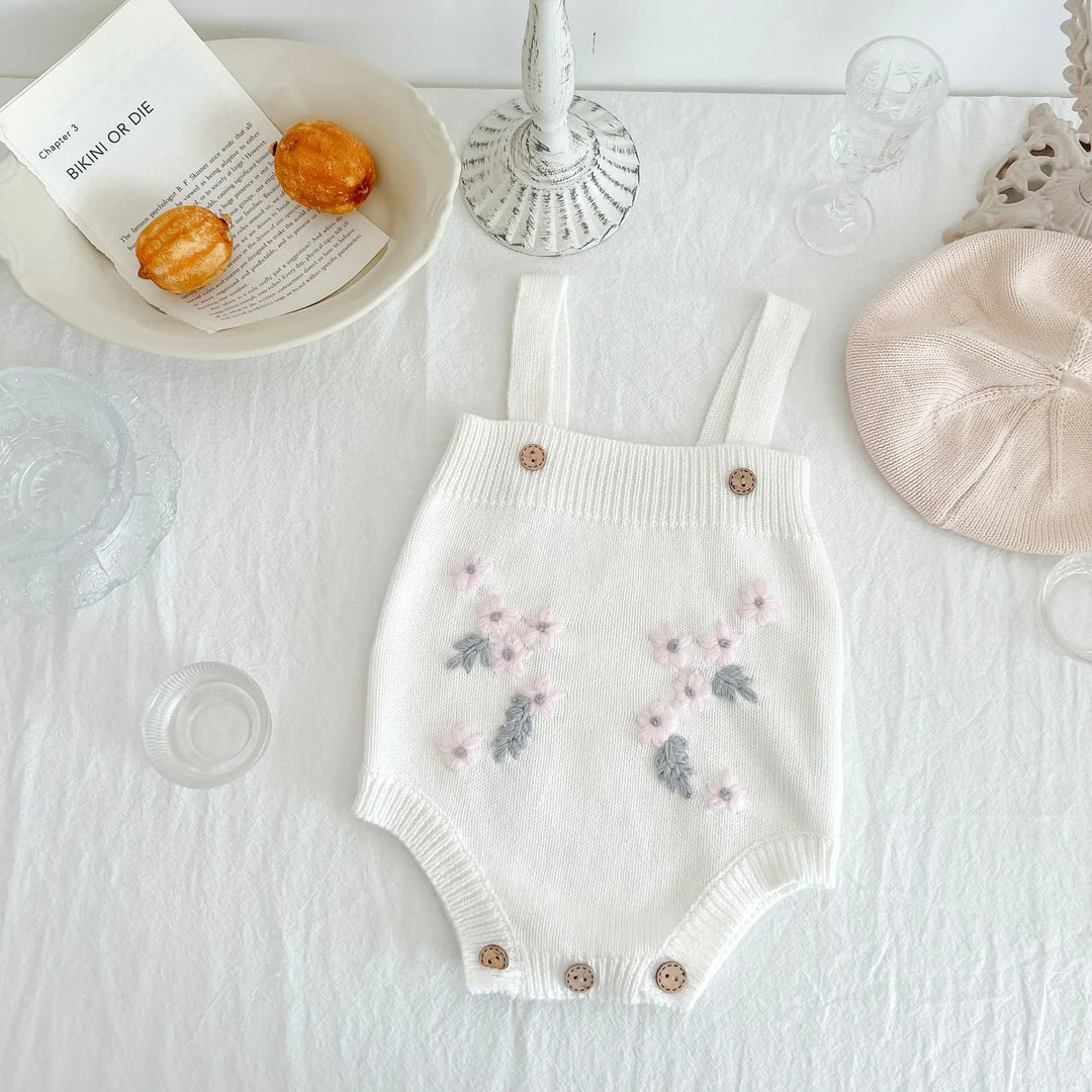White knitted baby romper with pink and gray floral embroidery on white tablecloth