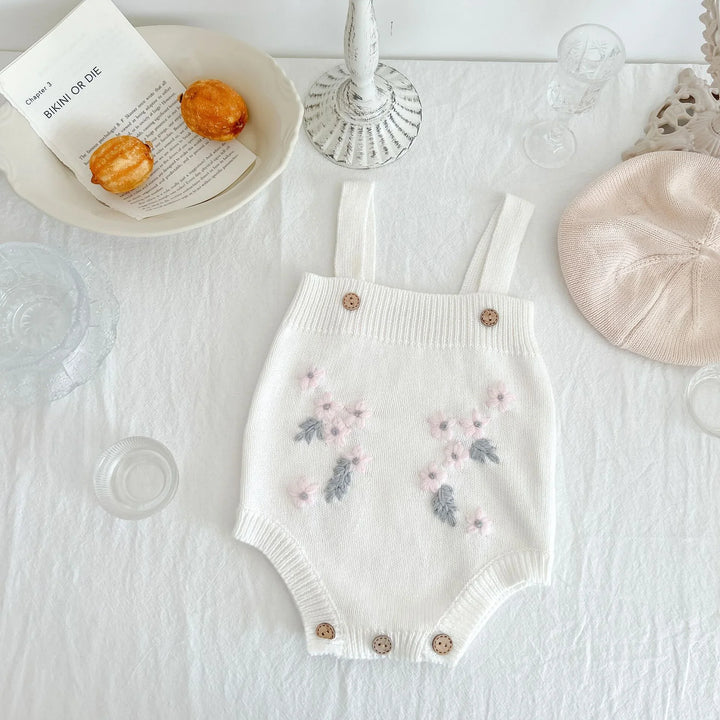 White knitted baby romper with pink and gray floral embroidery on white tablecloth
