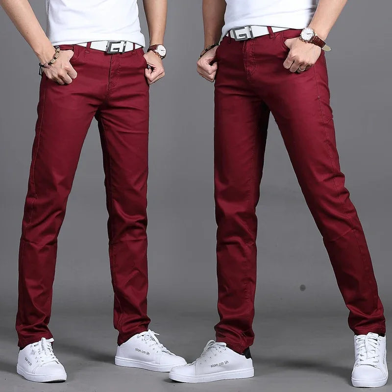 Men's slim fit burgundy pants paired with white sneakers, white belts, and wristwatches on gray background