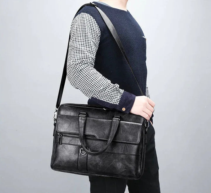 Man wearing navy sweater with checkered sleeves carrying black leather shoulder briefcase bag